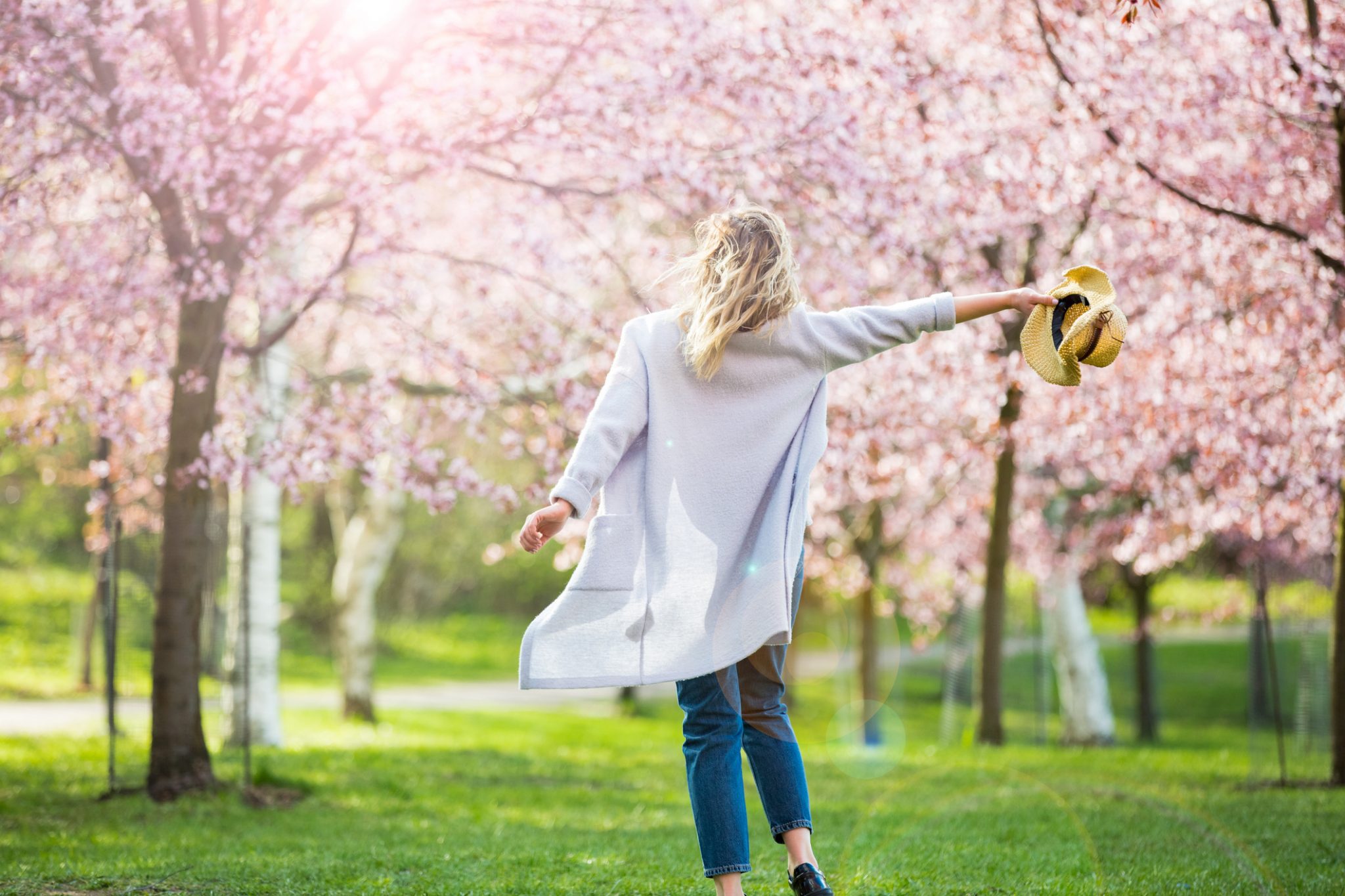 spring home buying, Young woman enjoying the nature in spring. Dancing, running and whirling in beautiful park with cherry trees in bloom. Happiness concept
