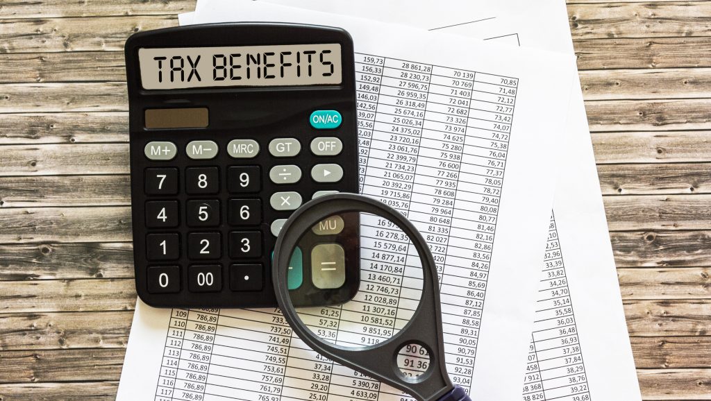 the inscription TAX BENEFITS on the display of the calculator, the documents are on a wooden table